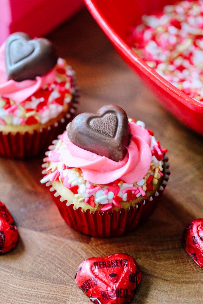 three cupcakes with hearts on them sitting on a wooden table next to some candy