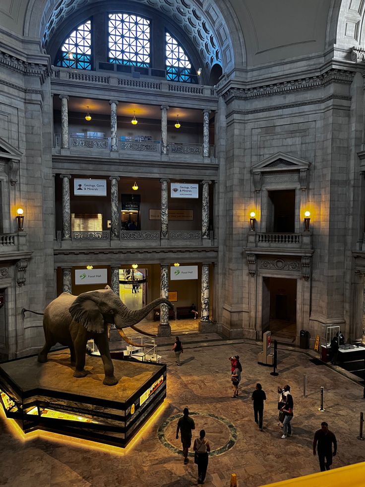 an elephant statue is in the middle of a large room with people walking around it