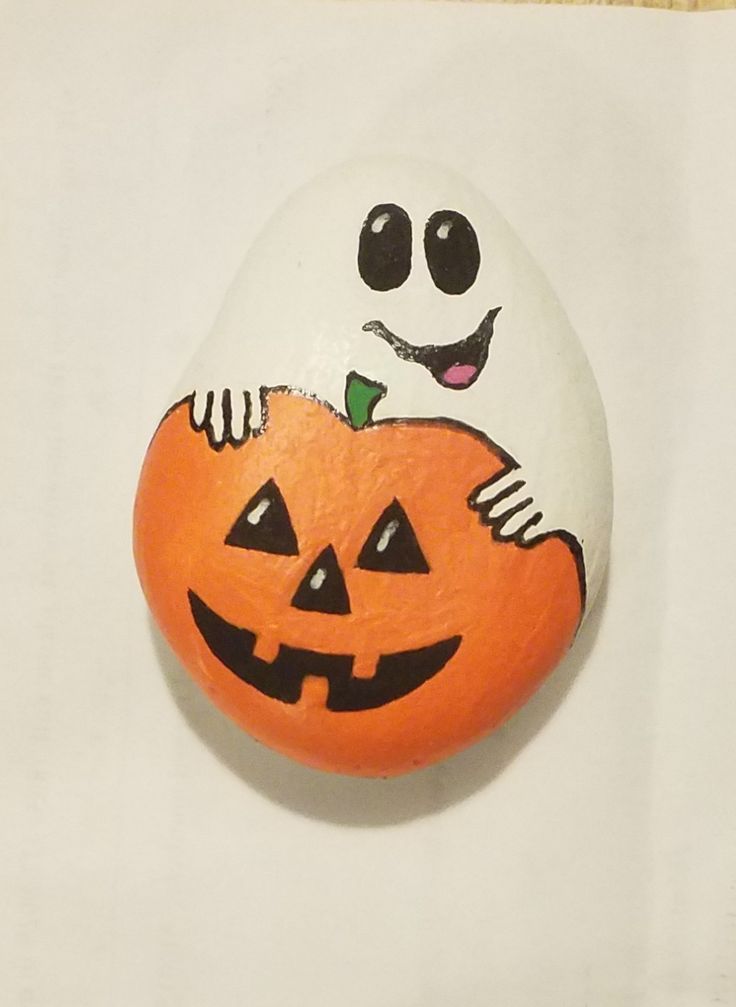 a painted rock with a jack - o'- lantern face on it, sitting on a white surface