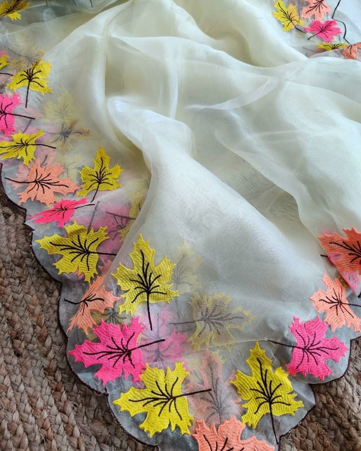 a white scarf with colorful flowers on it sitting on top of a carpeted floor