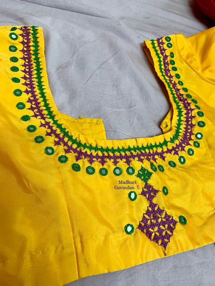 an embroidered yellow blouse with green and purple beads on the collar, sitting on a bed