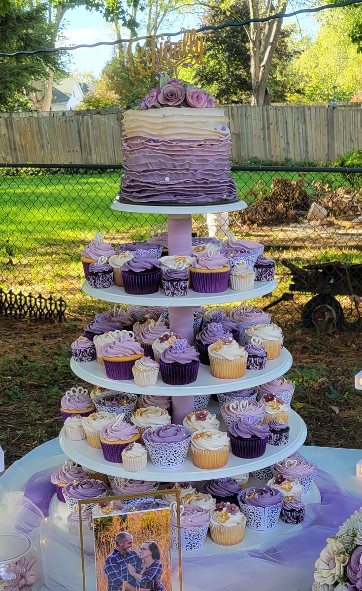 a tiered cake and cupcakes on a table