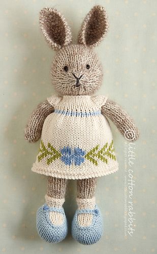 a knitted bunny wearing a dress and slippers is posed on a blue background