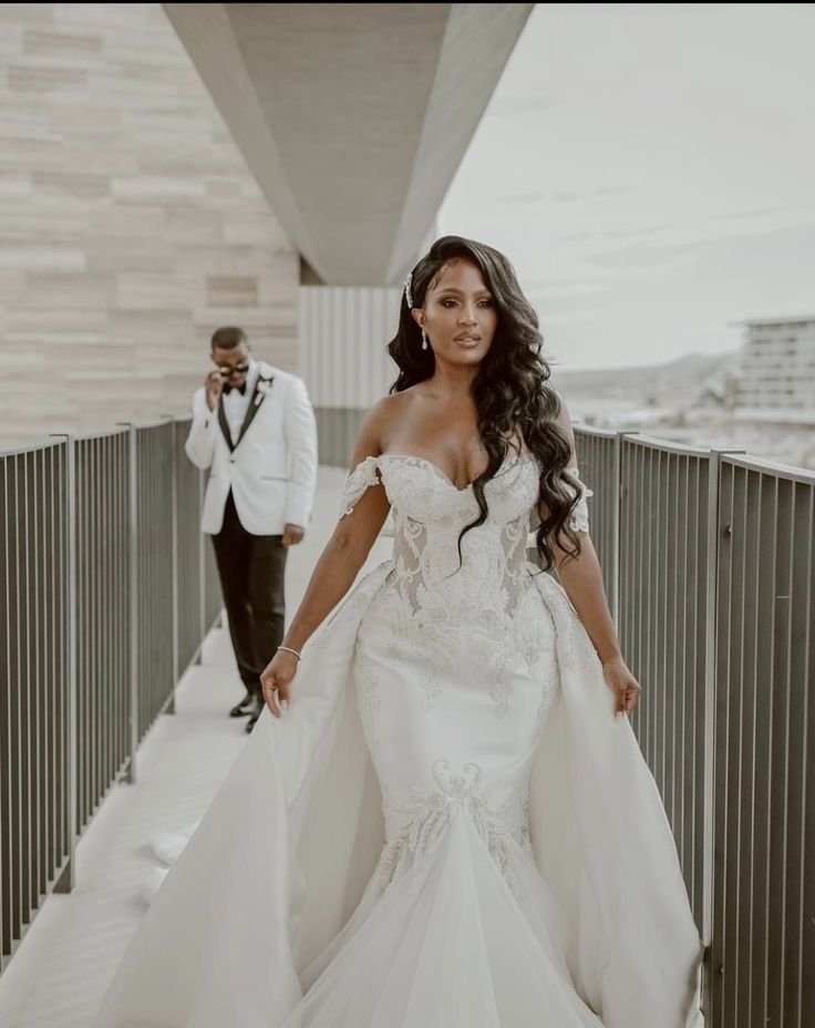 a woman in a wedding dress standing on a bridge next to a man wearing a tuxedo