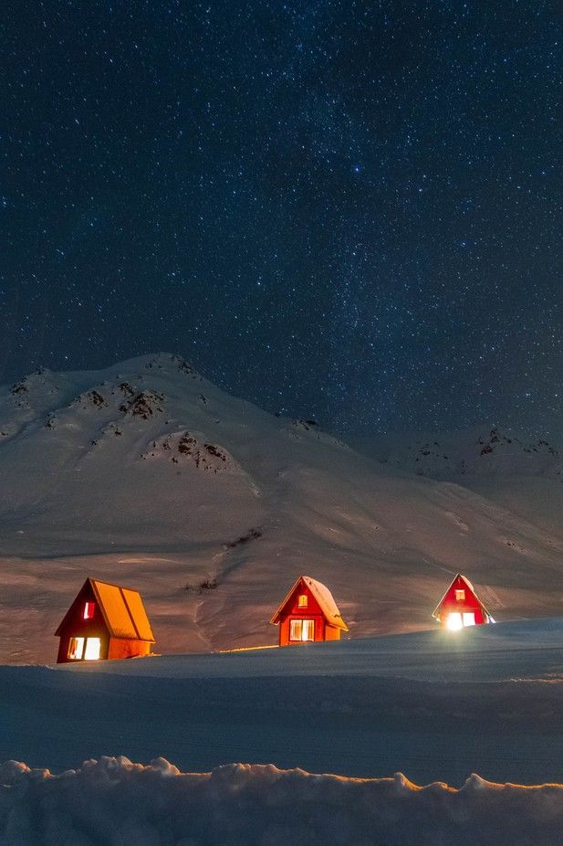 three small red houses sitting in the snow under a night sky with stars above them