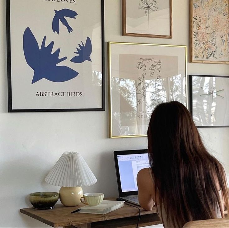 a woman sitting in front of a laptop computer on top of a desk next to pictures