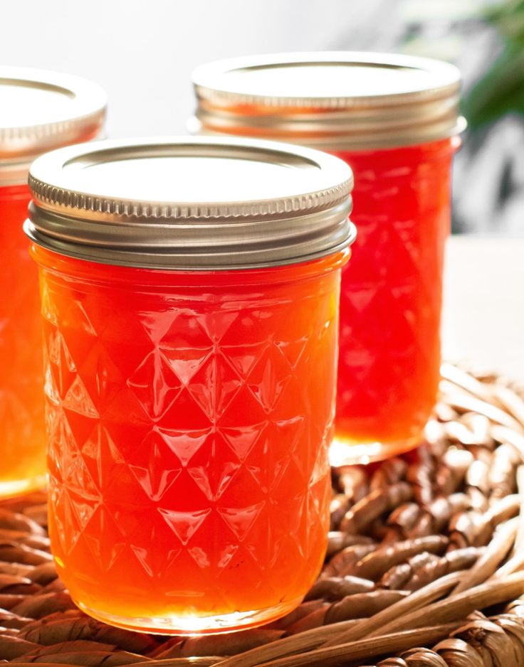 three jars filled with orange liquid sitting on top of a wicker basket next to pine cones