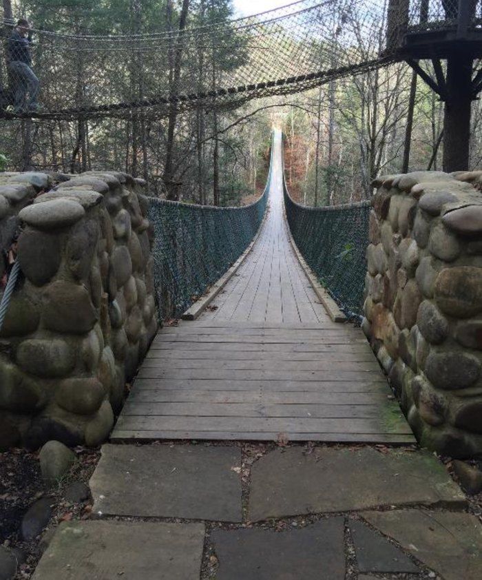 a bridge that is surrounded by trees and rocks on the sides, with a walkway leading up to it