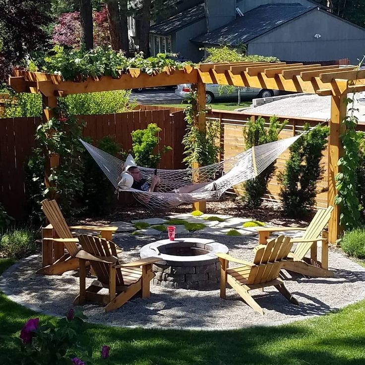 a hammock in the middle of a yard with two chairs and a fire pit