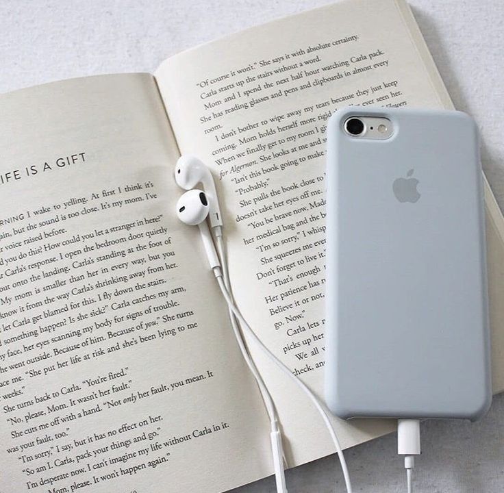 an open book with headphones and earbuds on it next to an iphone