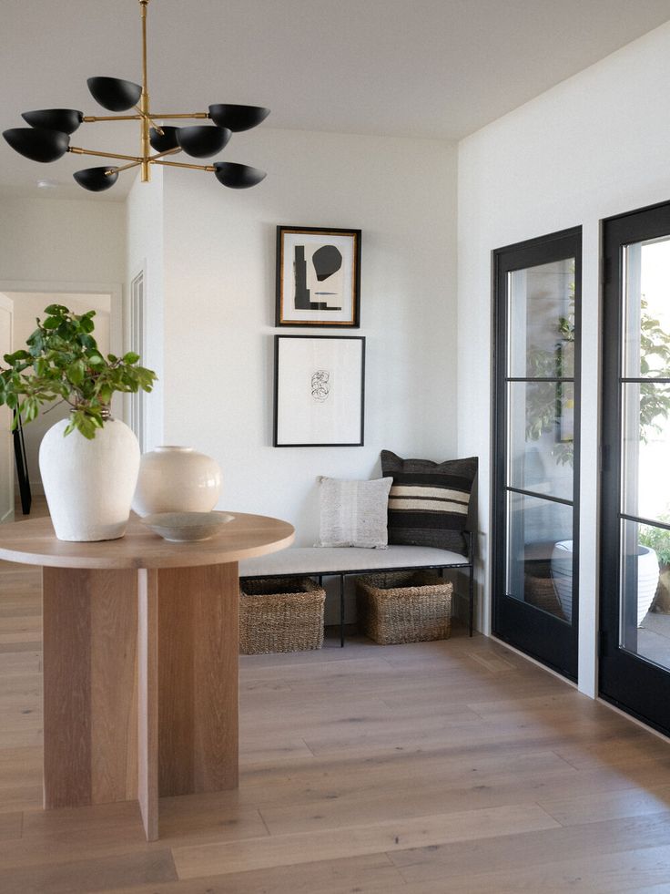 a living room filled with furniture next to a window covered in plants and framed pictures