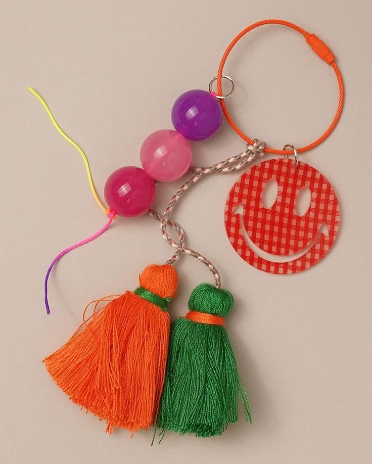 two tasselled key chains with smiley face and balloon attached to each one, on a white surface