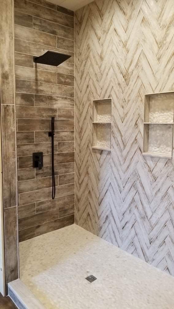 a walk in shower sitting next to a tiled wall with shelves on each side and an overhead shower head