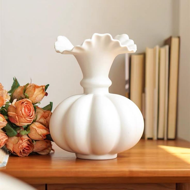 a white vase sitting on top of a wooden table next to a bouquet of flowers