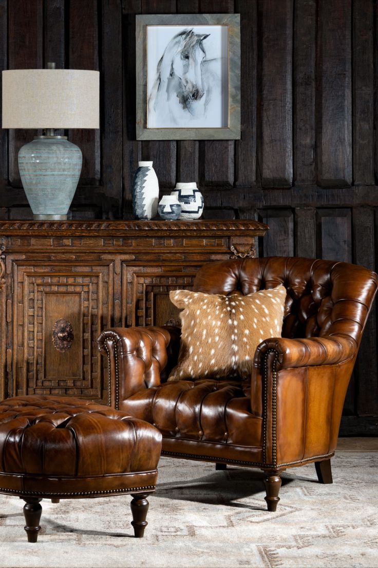 a brown leather chair and footstool in front of a wooden wall with pictures on it