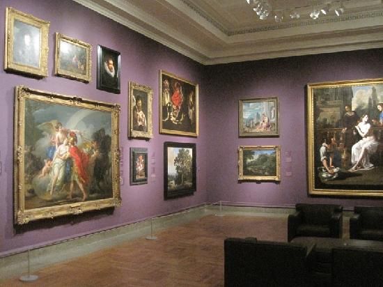 an art gallery with paintings on the wall and couches in front of purple walls