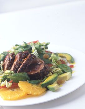 a white plate topped with meat and veggies next to sliced orange wedges