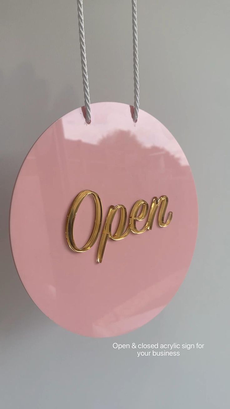 a pink round sign with the word open hanging from it's sides and two silver strings