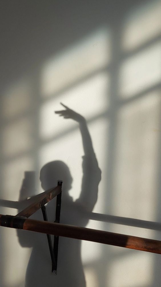 the shadow of a person standing in front of a window holding a skateboard and pointing at it