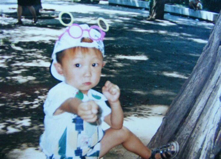 a young child sitting on the ground in front of a tree wearing sunglasses and a hat