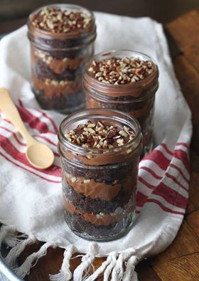 three mason jars filled with brownie and nuts on a towel next to a spoon