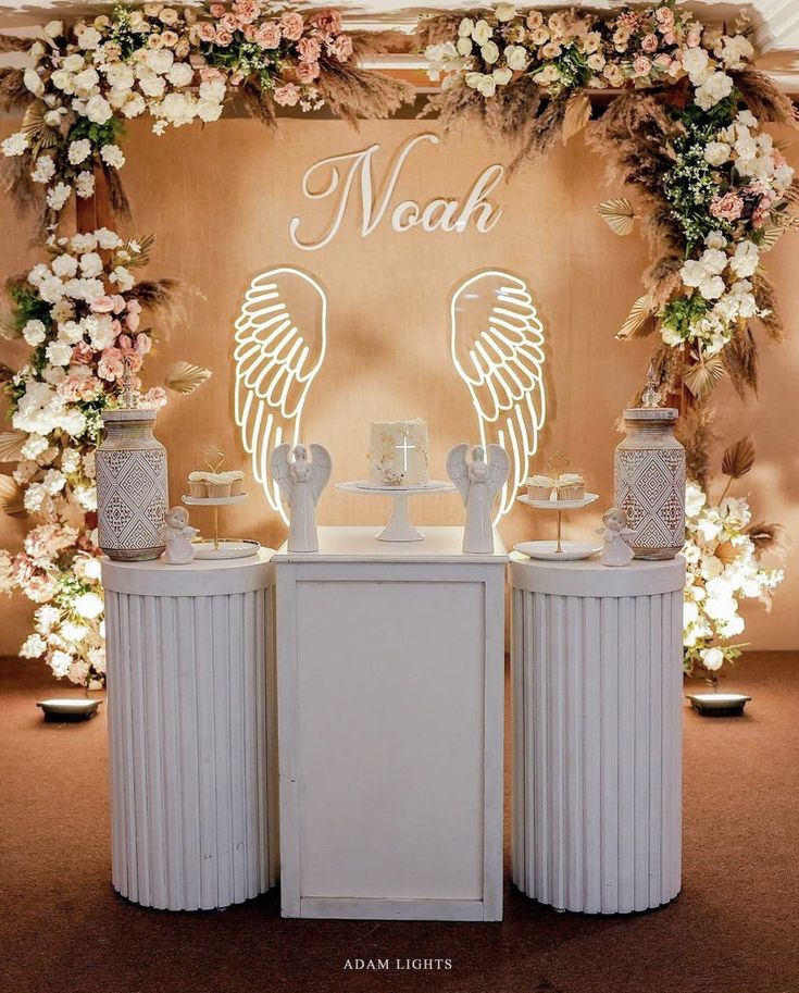 a white table topped with two vases filled with flowers and an angel decoration above it