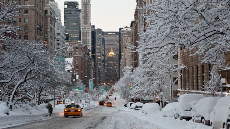 cars driving down a snow covered street with tall buildings in the backgrouds