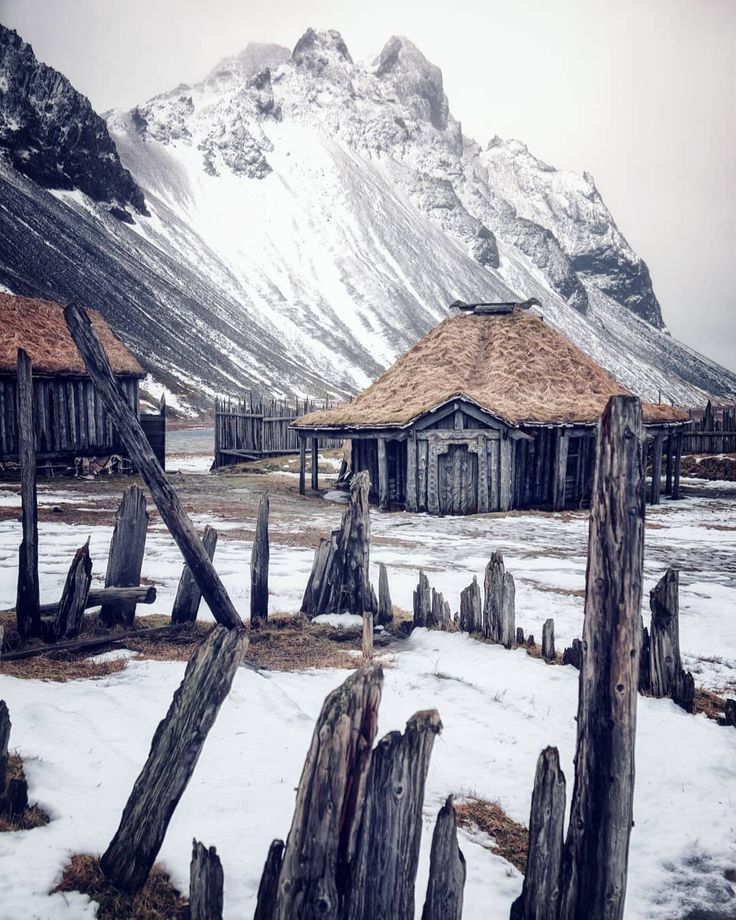 an old wooden shack in the snow with mountains in the background