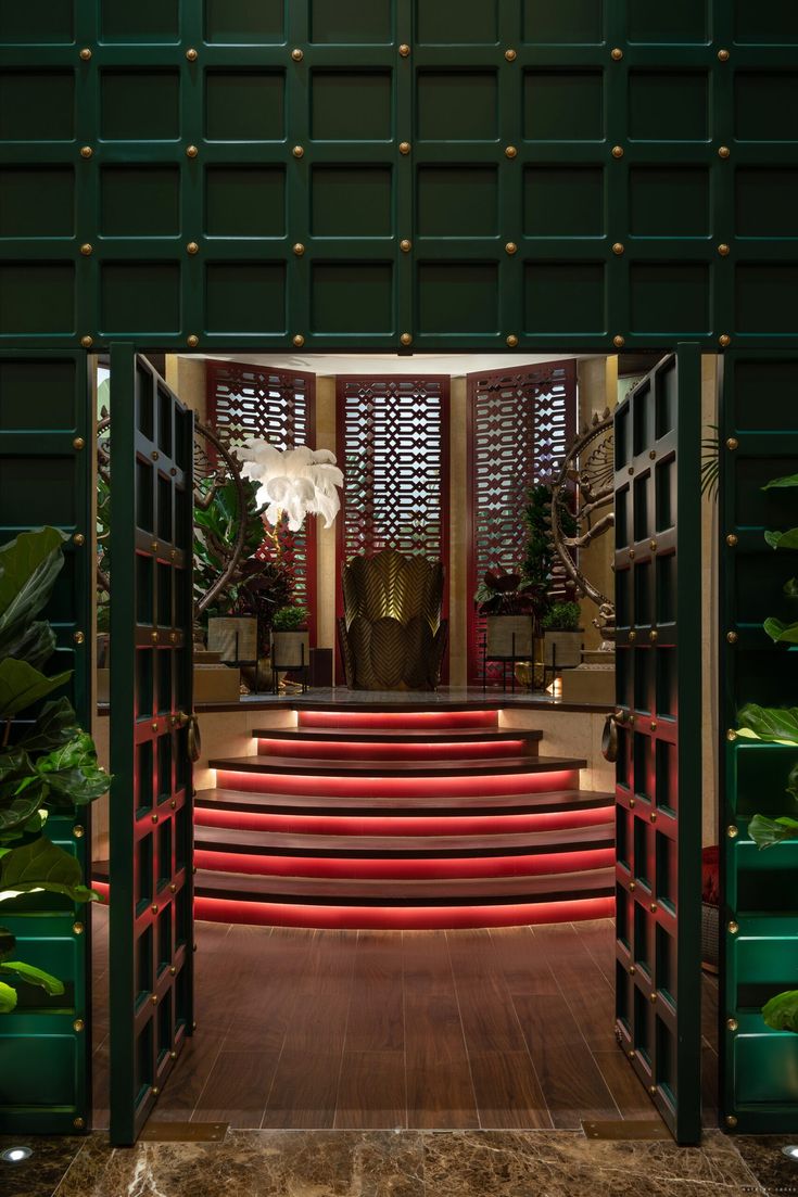 an open door leading to a set of stairs with red steps and green planters on either side