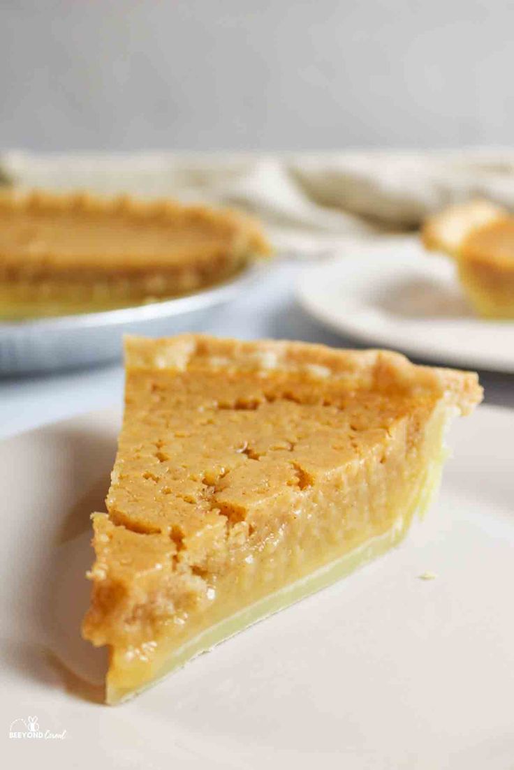 a slice of pumpkin pie on a white plate with other plates in the back ground