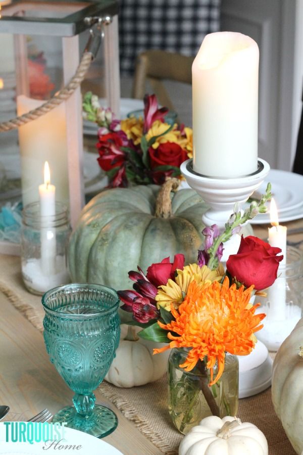 a table topped with vases filled with colorful flowers and candles next to pumpkins