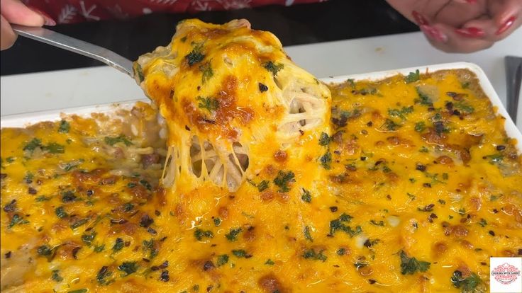 a person is holding a spoon over a casserole dish with cheese and meat