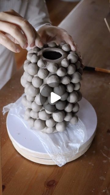 a person is making a vase out of balls on a white plate and wood table