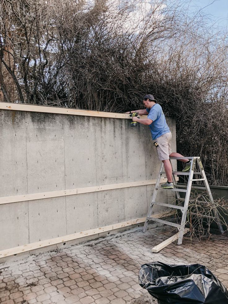 a man climbing up the side of a cement wall with a ladder on top of it