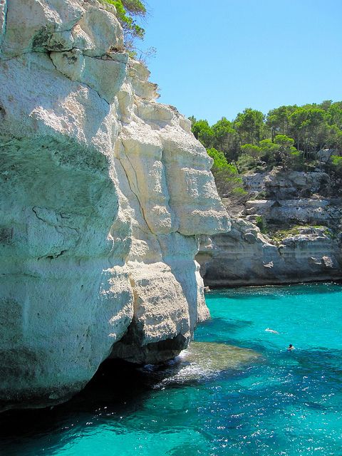 people are swimming in the clear blue water near some large rocks and trees on top of them