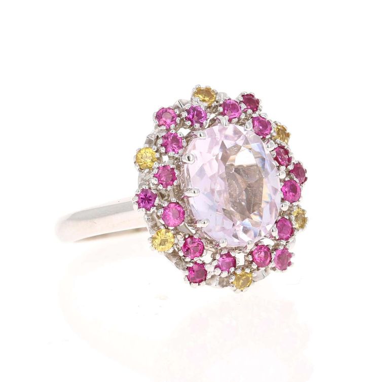 This beautiful ring has a Oval Cut 3.81 carat Kunzite that is set in the center of the ring and is surrounded by 24 Round Cut Pink and Yellow Sapphires that weigh 1.13 carats. The total carat weight of the ring is 4.94 carats. The Kunzite measures at 9 mm x 11 mm. The ring is made in 14K White Gold and weighs approximately 6.6 grams. Complimentary ring sizing is available upon request. Oval White Sapphire Ring, Oval White Sapphire Ring With Center Stone, Oval White Sapphire Ring With Halo Setting, Dazzling Oval Multi-stone Cluster Ring, White Oval Sapphire Gemstone Ring, White Oval Sapphire Ring With Center Stone, Luxury White Sapphire Oval Ring, Pink Round Amethyst Ring Fine Jewelry, Exquisite Pink Sapphire Round Rings