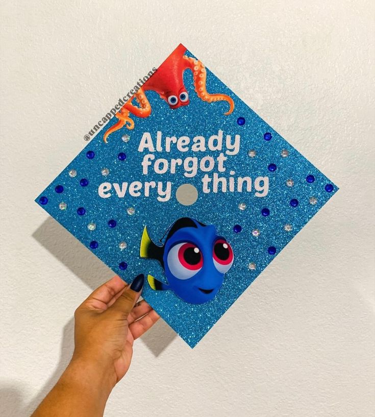 someone holding up a blue graduation cap with an image of finding nemo on it