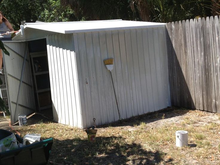 a small white shed sitting in the middle of a yard next to a wooden fence