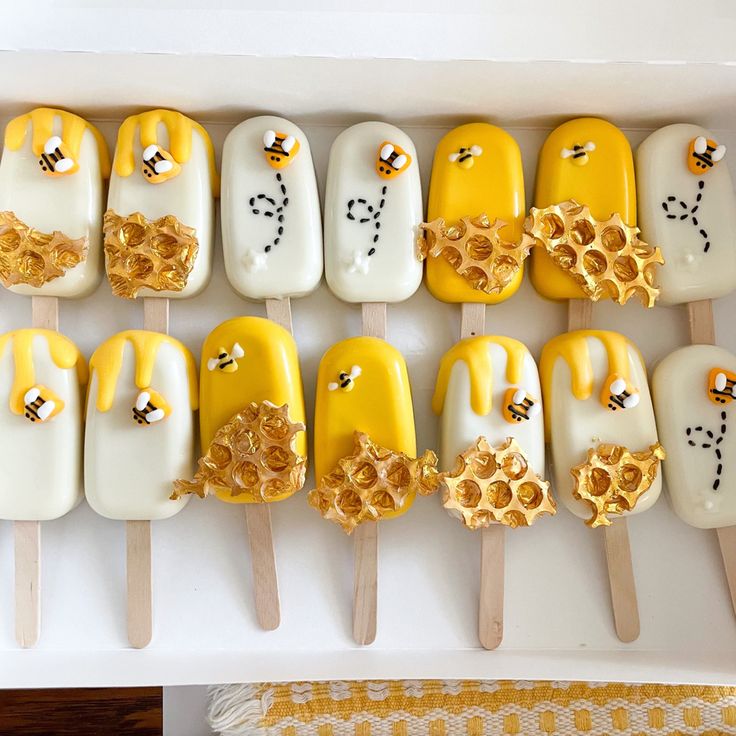 there are many yellow and white pops with bees on them in a box next to a table