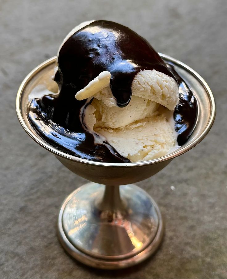 an ice cream sundae with chocolate sauce in a silver bowl on a table top