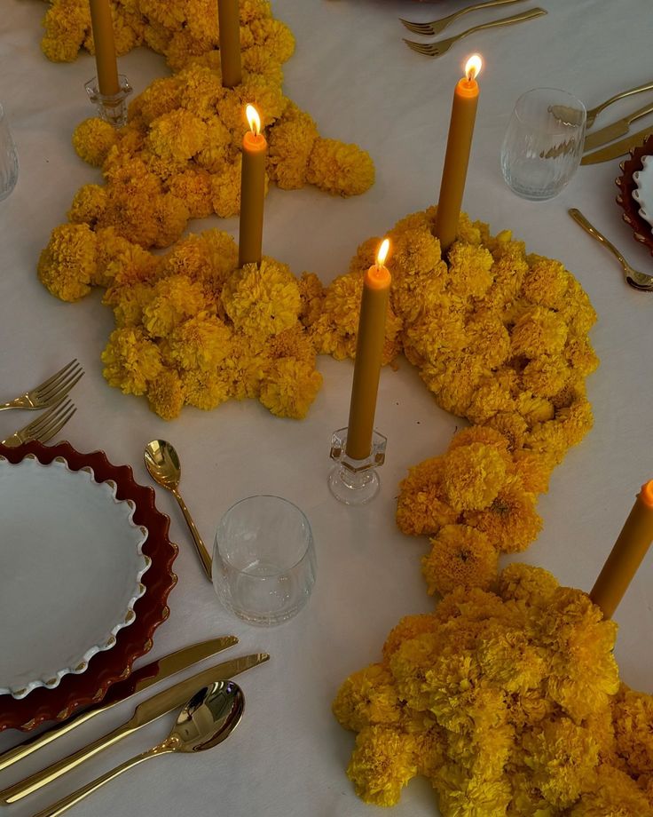 a table topped with lots of yellow flowers next to silverware and candles on top of plates