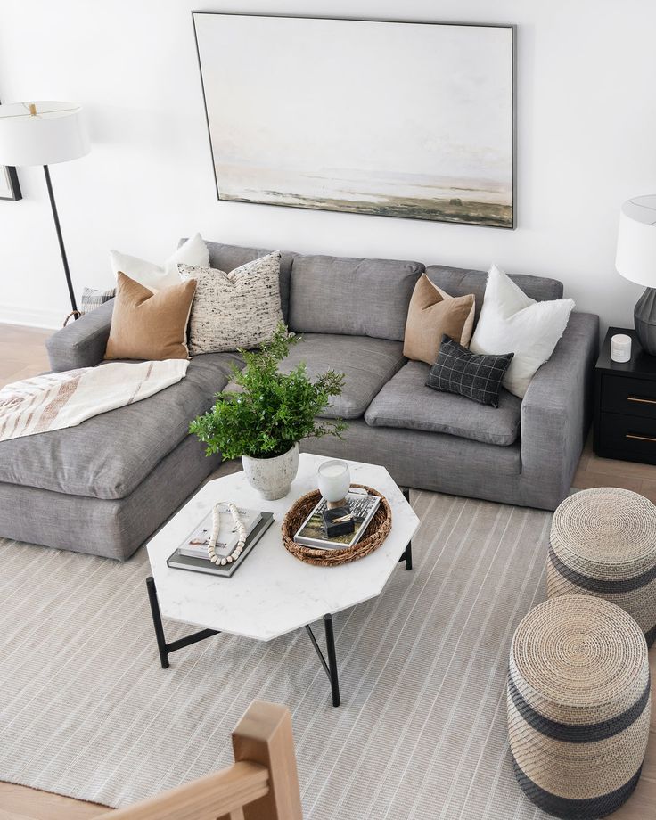 a living room with grey couches and white coffee table in the middle, surrounded by wicker baskets