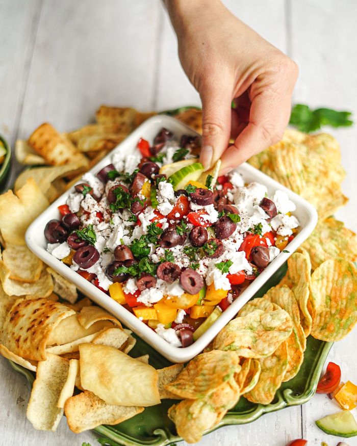 a person dipping olives into a bowl filled with tortilla chips and salsa