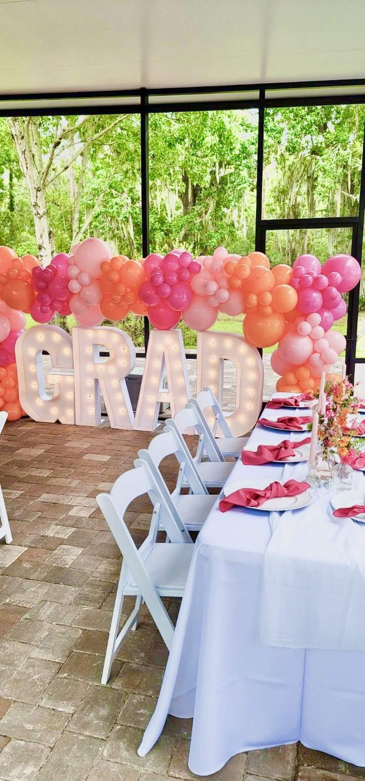 a table set up for a graduation party with pink and orange balloons on the wall