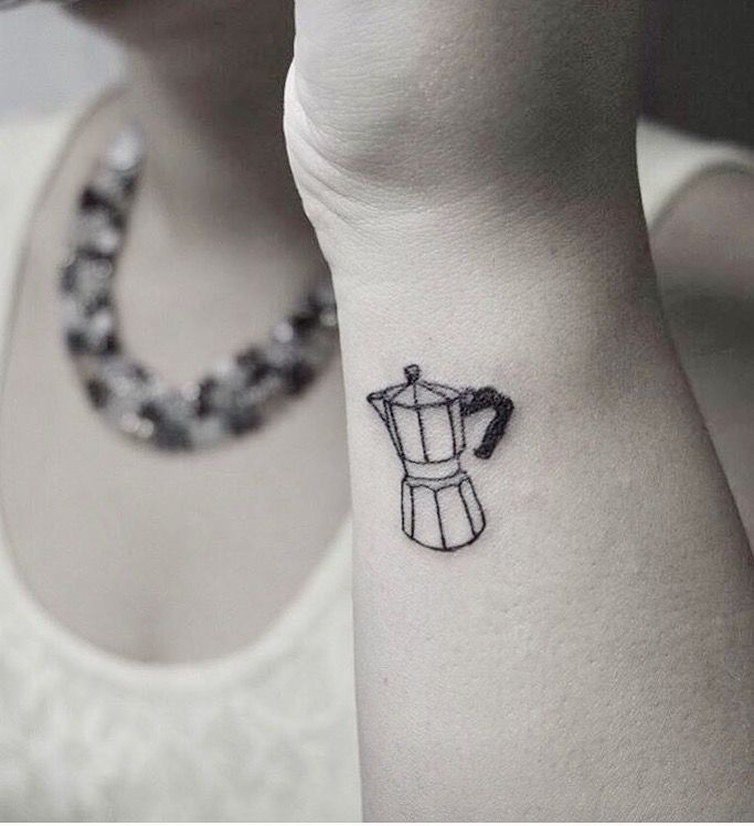 a small tattoo on the wrist of a woman with a coffee pot in front of her