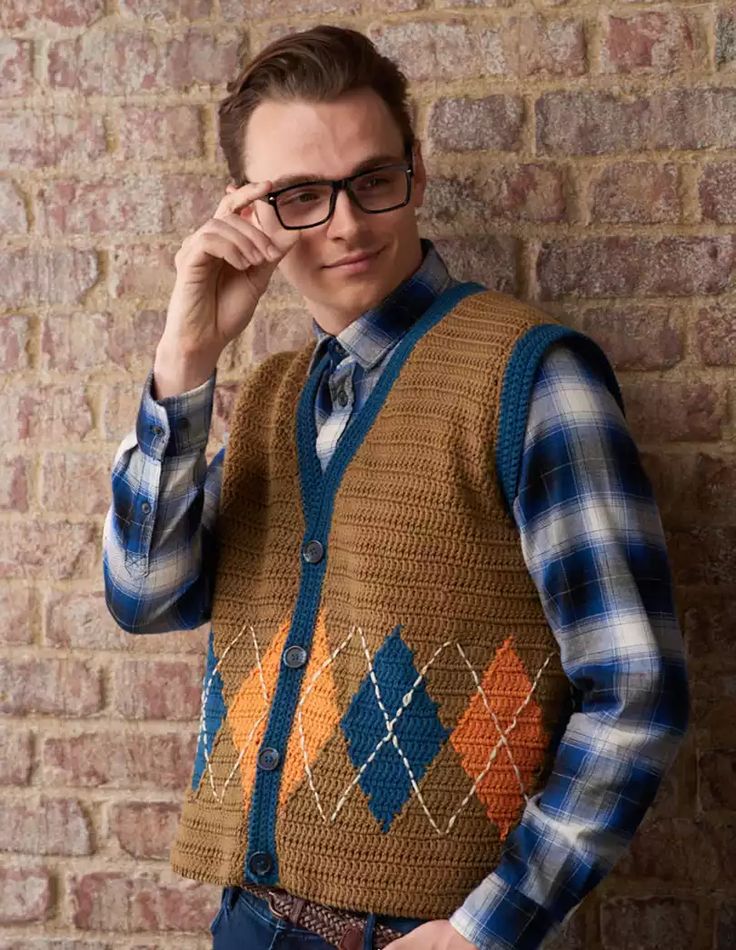 a man wearing glasses and a sweater vest standing in front of a brick wall with his hand on his head