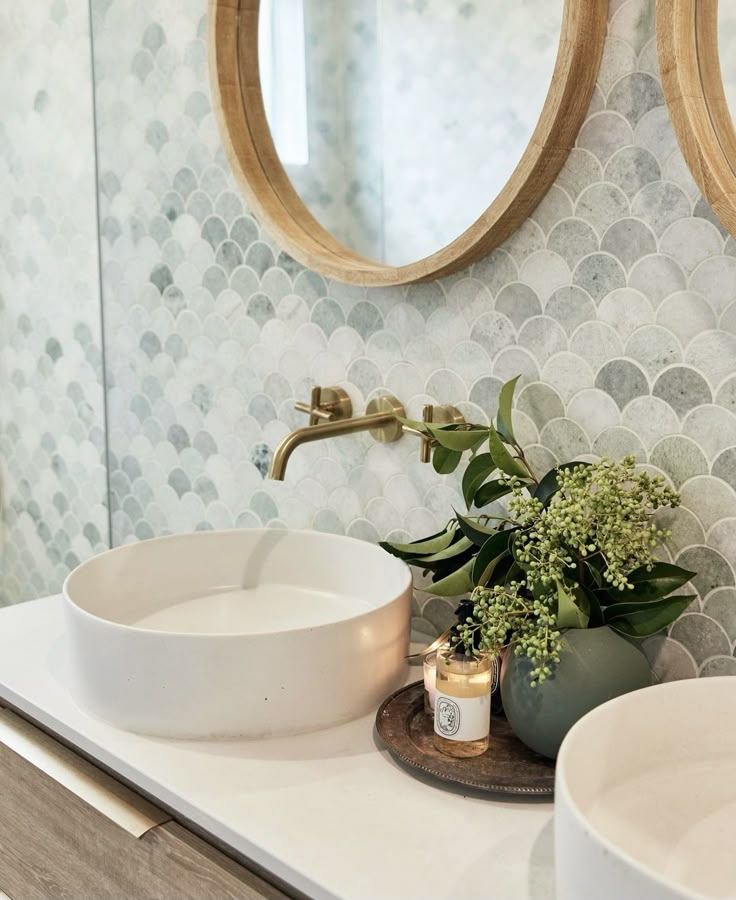 two round mirrors are above the sink in this bathroom with white countertops and wood accents