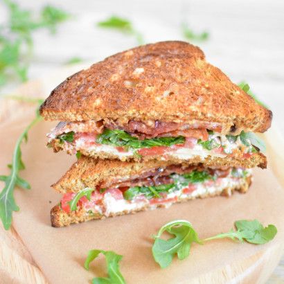 a grilled sandwich with meat, cheese and greens on a cutting board next to some parsley