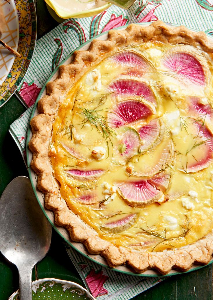 a tart dish with radishes and other food items around it on a table