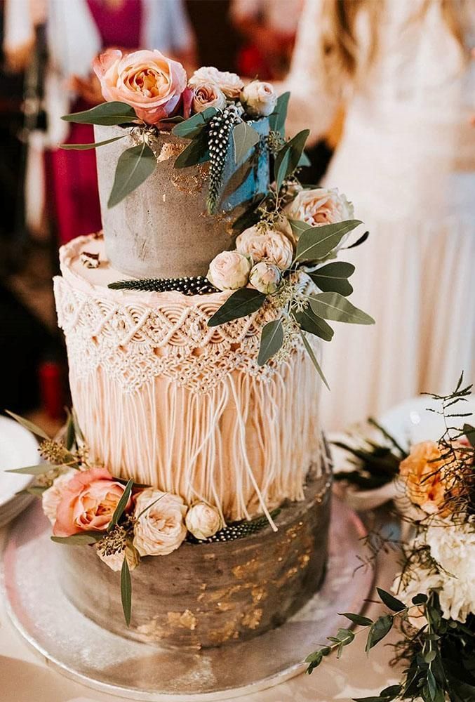 a three tiered wedding cake with flowers and greenery on the top is surrounded by other floral arrangements